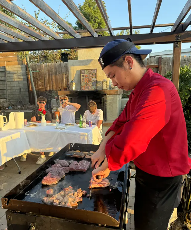 The chef slices steak on a loaded griddle at golden hour